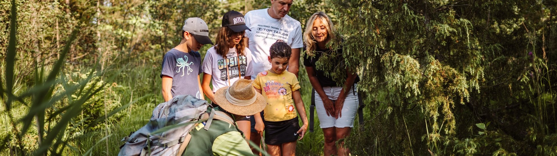 Eine 5-köpfige Familie schaut in einem Waldgebiet interessiert auf einen Naturschutzranger in grüner Kleidung mit Strohhut, der auf etwas im Gras zeigt., © Tölzer Land Tourismus|Leonie Lorenz Eine 5-köpfige Familie schaut in einem Waldgebiet interessiert auf einen Naturschutzranger in grüner Kleidung mit Strohhut, der auf etwas im Gras zeigt., © Tölzer Land Tourismus|Leonie Lorenz