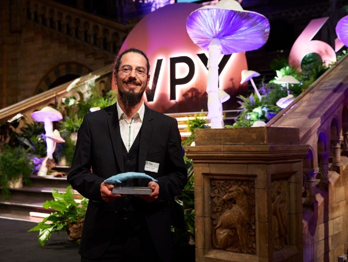 Im dunklen Anzug steht der stolz lächelnde Preisträger mit dem Award - einer Blauwal-Figur- im Naturhistorischen Museum London, © The Trustees of the Natural History Museum, London Im dunklen Anzug steht der stolz lächelnde Preisträger mit dem Award - einer Blauwal-Figur- im Naturhistorischen Museum London, © The Trustees of the Natural History Museum, London