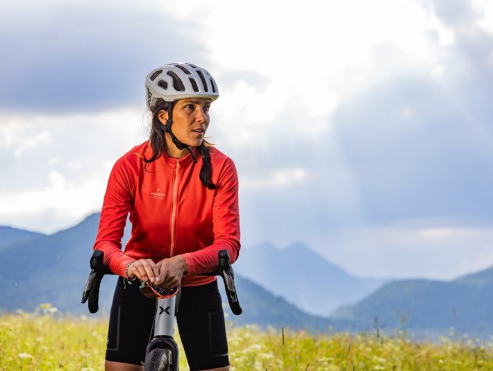 Bitte nutze die ausgewiesenen Wege.
Das Bild zeigt: Eine Frau mit Fahrradhelm und roter Sportjacke lehnt an ihrem Fahrrad, blickt nach rechts. Sie steht auf einer Blumenwiese vor einer Bergkulisse. Sonnenstrahlen brechen durch die Wolken am Himmel und beleuchten die Szene stimmungsvoll., &copy; T&ouml;lzer Land Tourismus|farmhouse7
