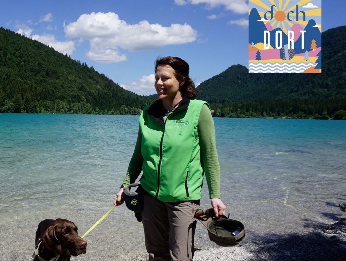 Rangerin Sabine Gerg mit ihrem Hund am Walchensee  - mit dem Podcastlogo von dochdort, Lisa Steinbacher, &copy; T&ouml;lzer Land Tourismus|KUNZ PR