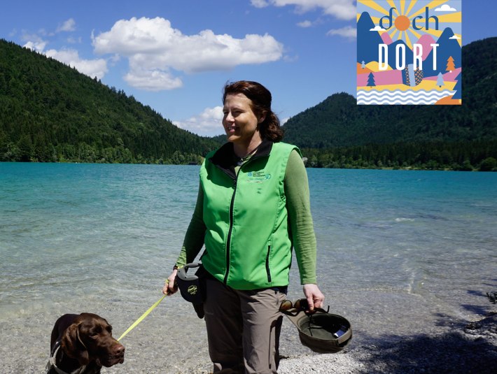Rangerin Sabine Gerg mit ihrem Hund am Walchensee  - mit dem Podcastlogo von dochdort, Lisa Steinbacher, &copy; T&ouml;lzer Land Tourismus|KUNZ PR