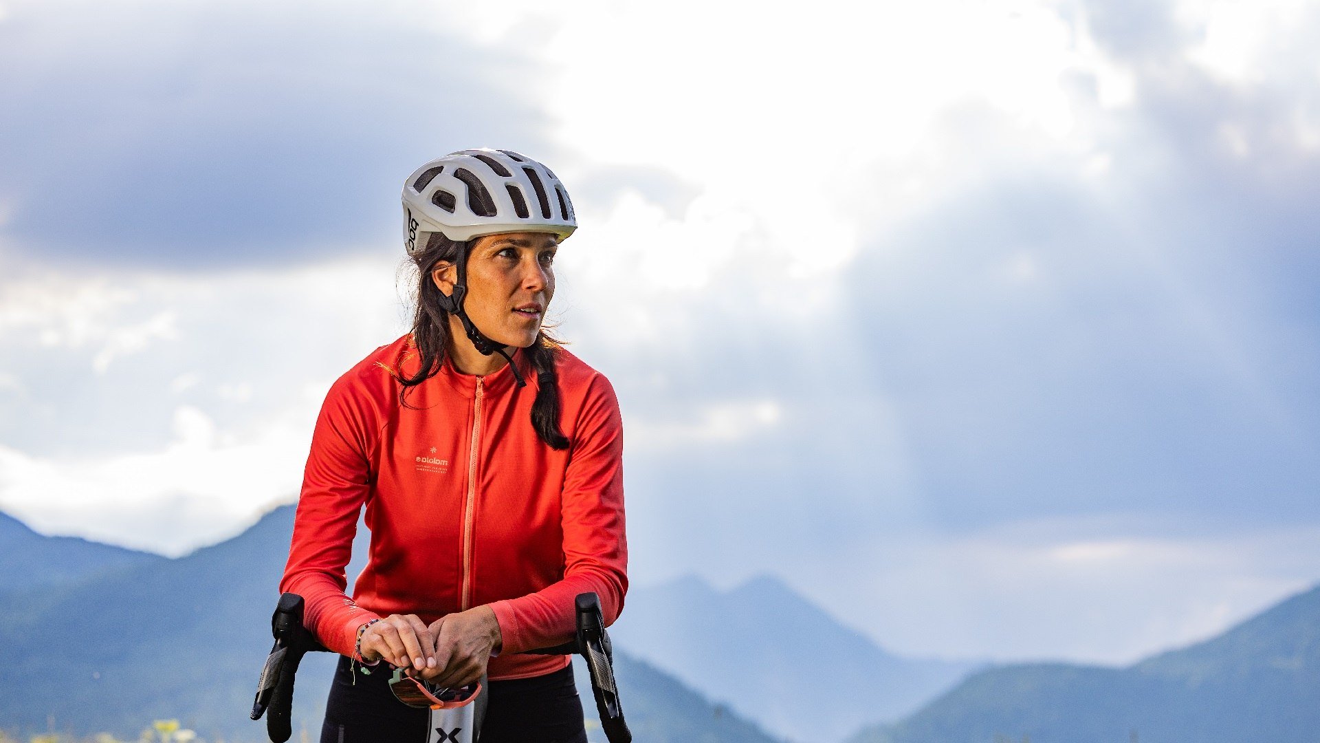 Bitte nutze die ausgewiesenen Wege.
Das Bild zeigt: Eine Frau mit Fahrradhelm und roter Sportjacke lehnt an ihrem Fahrrad, blickt nach rechts. Sie steht auf einer Blumenwiese vor einer Bergkulisse. Sonnenstrahlen brechen durch die Wolken am Himmel und beleuchten die Szene stimmungsvoll., © Tölzer Land Tourismus|farmhouse7
